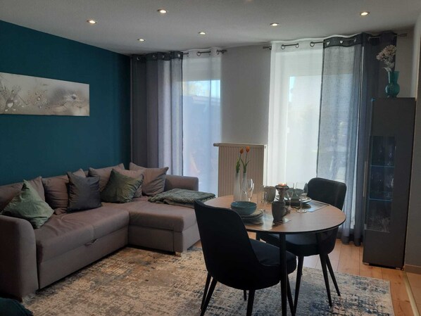 A living room with a sofa, a dining table with chairs, a vase with flowers, and a radiator.