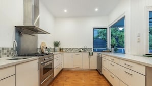 A modern kitchen with white cabinetry, a stainless steel range hood, a built-in oven, and a large window providing natural light.