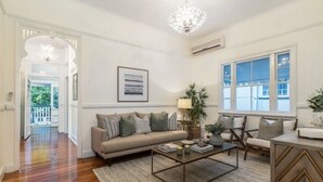 A living room with a sofa, coffee table, and chairs. There is a chandelier, a window, and a door leading to a balcony.