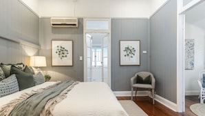 A bedroom with a bed, a chair, and two wall-mounted air conditioners.