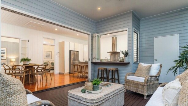 A spacious living area with a wooden deck, wicker furniture, and a kitchen in the background.