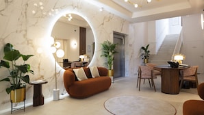 A modern living room with a marble wall, a round mirror, a brown sofa, a coffee table, and a dining area with chairs and a lamp.