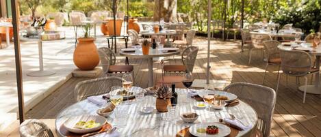 An outdoor dining area with round tables, wicker chairs, and umbrellas.