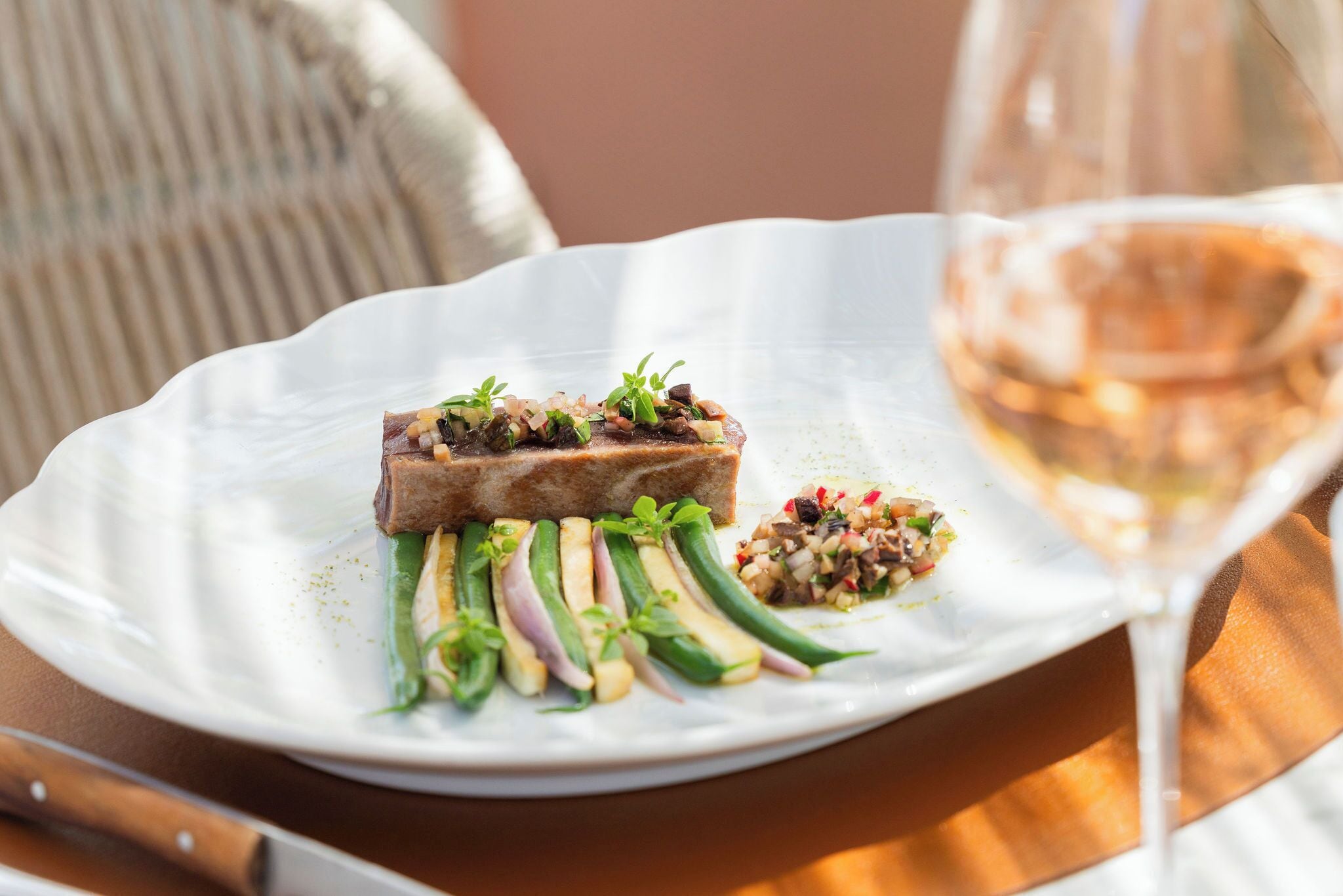 Une assiette blanche contenant un plat de viande, des légumes verts et une petite salade, accompagnée d’un verre de vin.