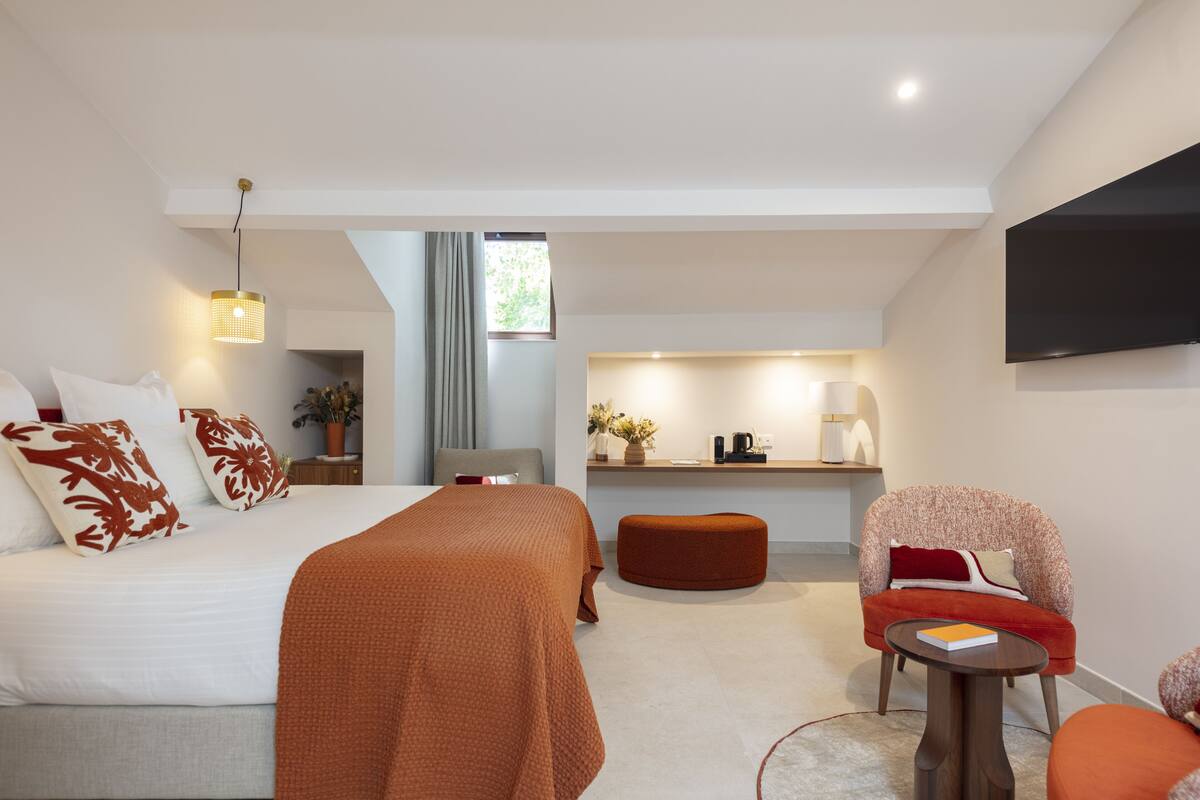 Ein modernes Hotelzimmer mit einem großen Bett, einer Sitzecke, einer Küchenzeile und einem an der Wand montierten Fernseher.