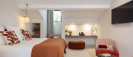 Una habitación de hotel moderna con una cama grande, una zona de estar, una kitchenette y un televisor montado en la pared.