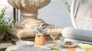 Una mesa redonda con mantel blanco, rodeada por una silla blanca, una planta en maceta y una copa de vino blanco.