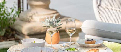 A round table with a white tablecloth, surrounded by a white chair, a potted plant, and a glass of white wine.