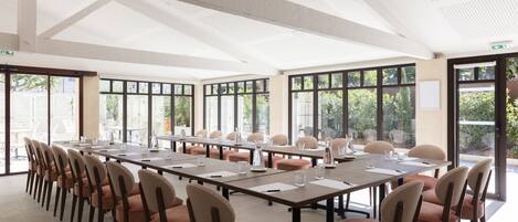 A conference room with long tables and chairs, large windows, and a high ceiling.