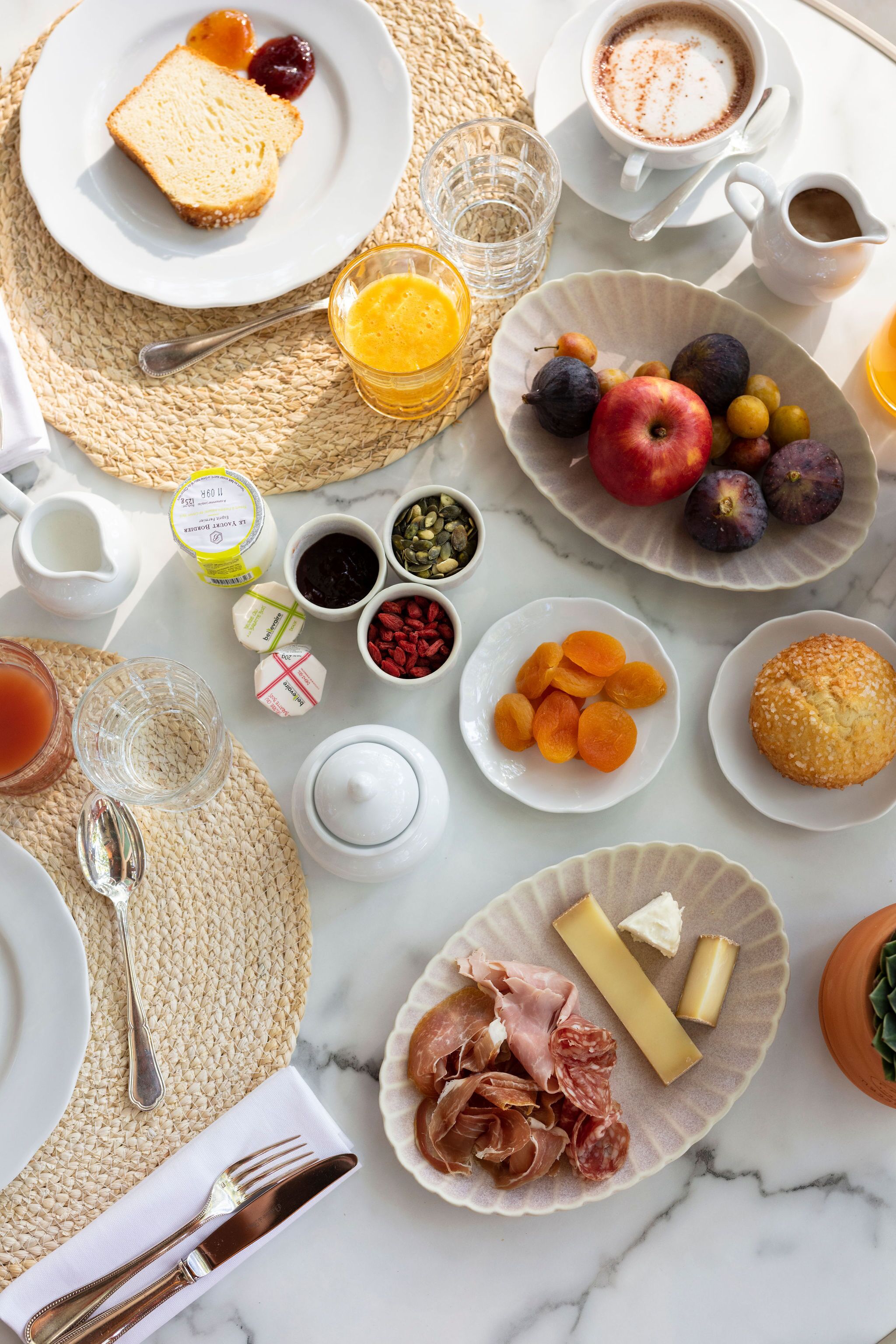 A breakfast setting with various food items and beverages on a marble table.