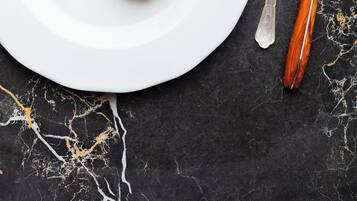 Prato branco com um prato de legumes coloridos, uma colher e uma faca sobre uma superfície de mármore escuro.