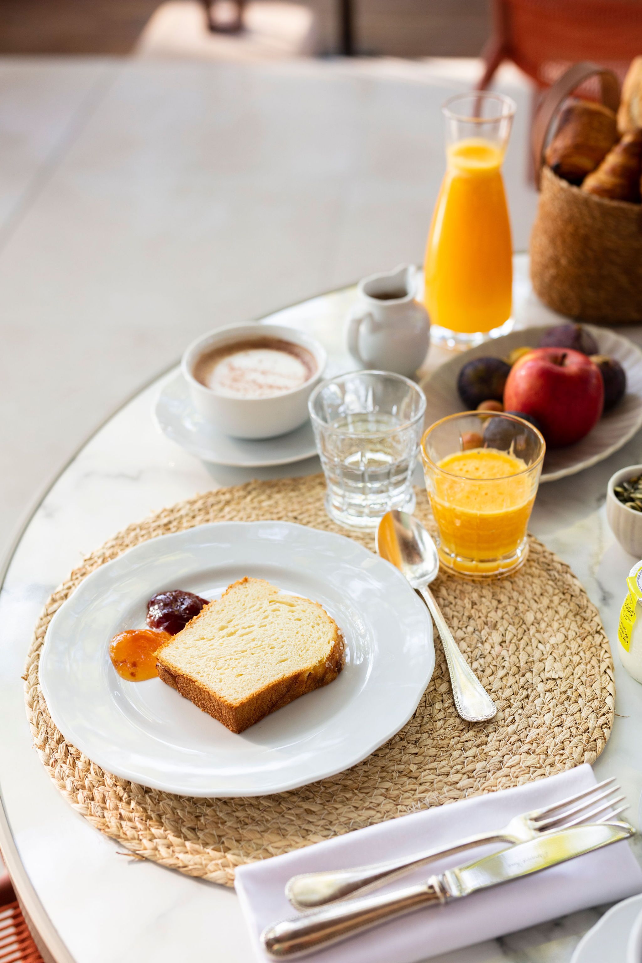 Desayuno con tostadas, mermelada, un vaso de zumo de naranja, un tazón de sopa y una fuente de fruta.