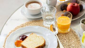 Desayuno con tostadas, mermelada, un vaso de zumo de naranja, un tazón de sopa y una fuente de fruta.