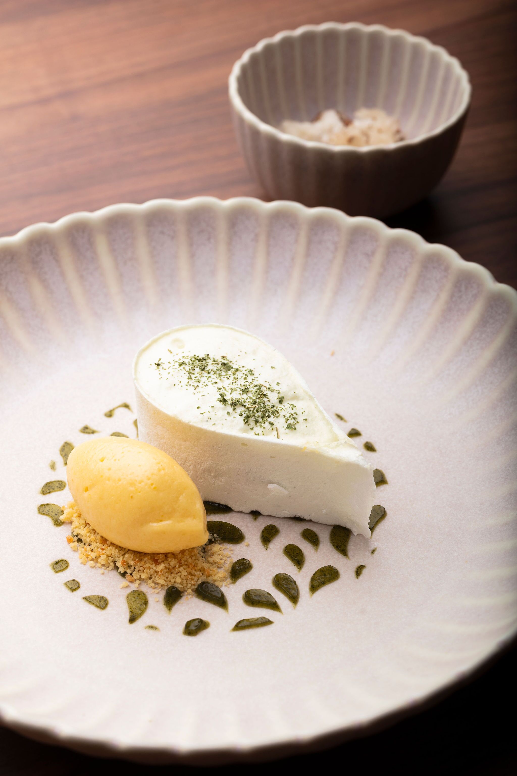 A dessert on a plate with a scoop of ice cream and a small bowl in the background.