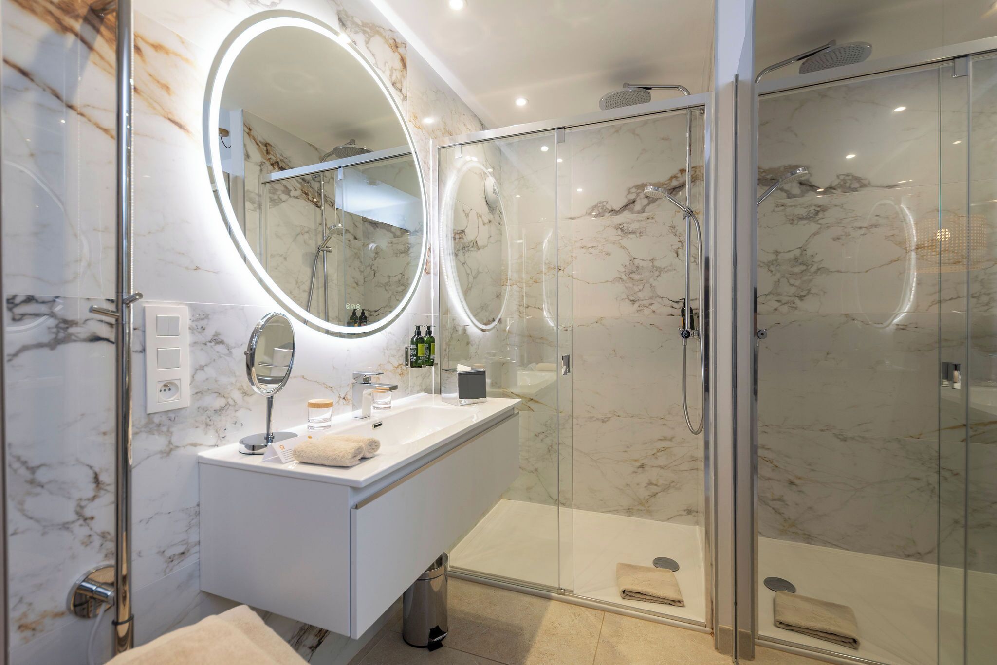 Een moderne badkamer met een marmeren wastafel, een grote spiegel en een douche met glazen wanden.