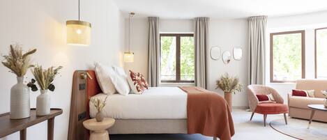 Un dormitorio moderno con cama, mesitas de noche, una silla, un sofá y un ventanal con cortinas.
