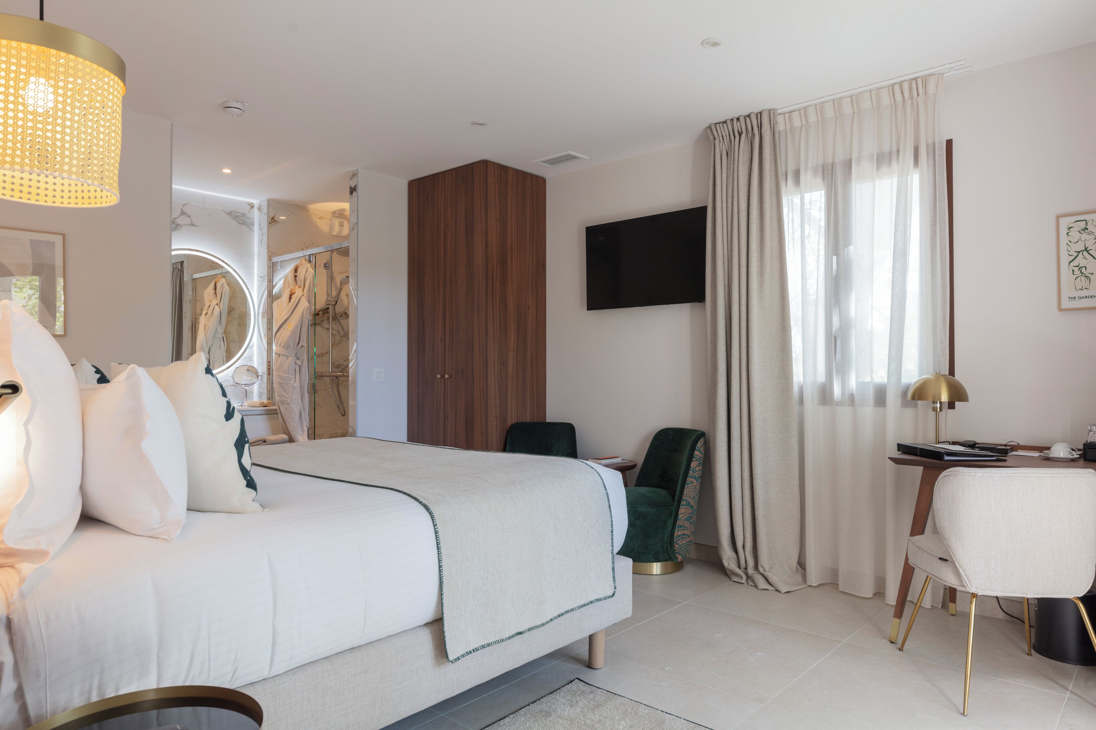 Ein modernes Hotelzimmer mit einem großen Bett, einem Schreibtisch, einem Sessel, einem Fernseher und einem großen Fenster mit Vorhängen.