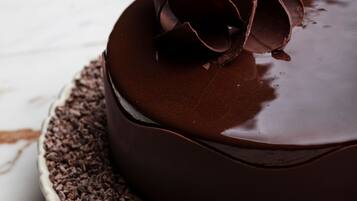 A chocolate cake with a glossy finish on a white plate, surrounded by chocolate shavings.