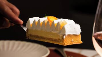 Une part de gâteau recouverte de glaçage blanc et décorée de tranches d’orange, présentée sur une assiette.