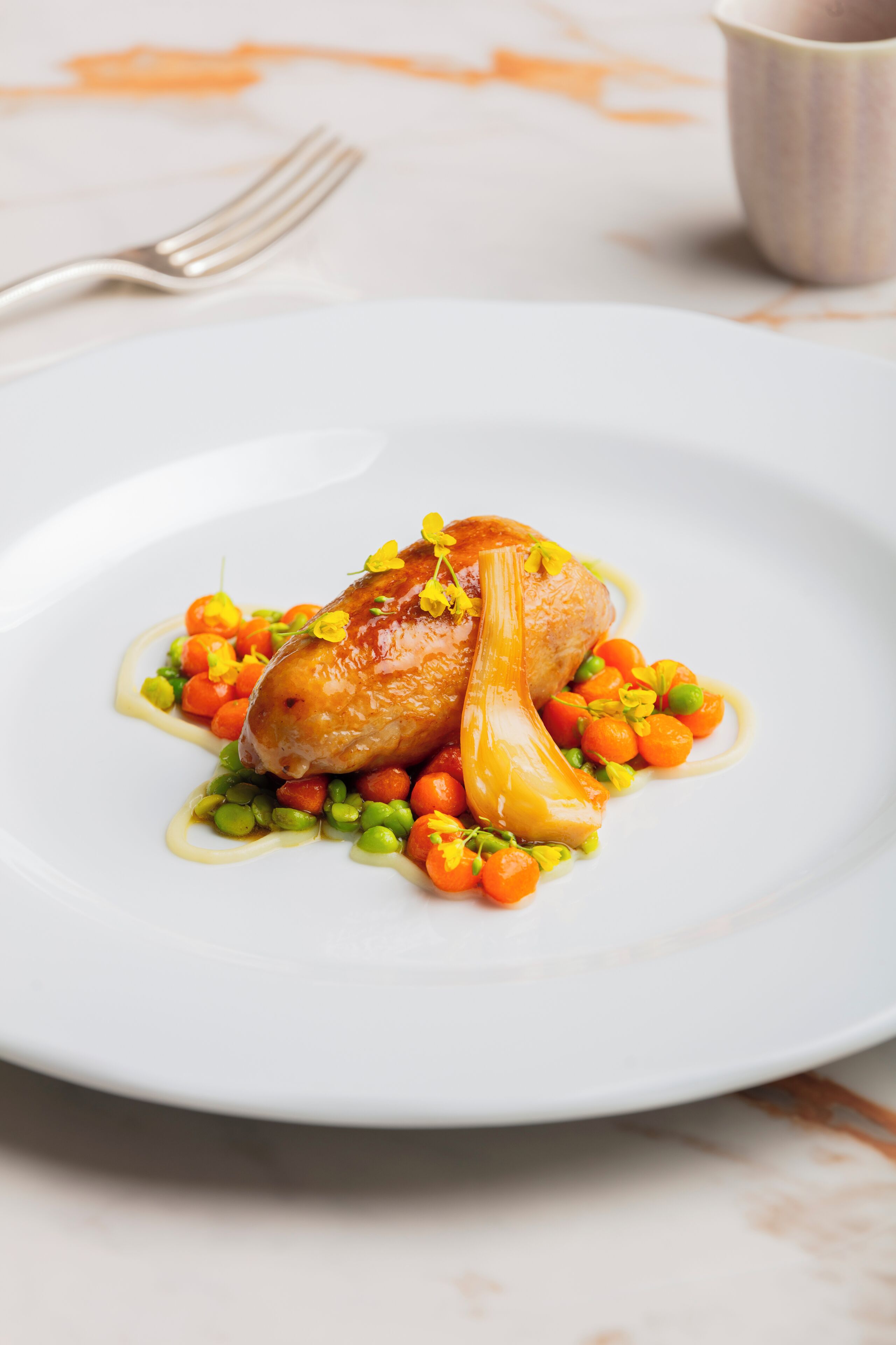 A white plate with a roasted chicken, peas, carrots, and a sauce.