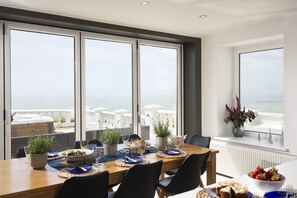 Ein Essbereich mit Blick auf das Meer, ein Holztisch gedeckt mit Tellern, Gläsern und Topfpflanzen.