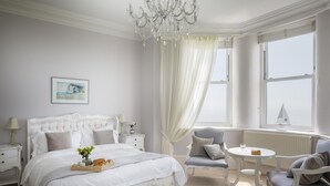 Ein Schlafzimmer mit einem großen Bett, einem Chandelier, einem Fenster mit Blick und einem kleinen Tisch mit Stuhl.