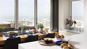 Ein Essbereich mit Tisch für vier Personen, der auf einen Balkon mit weißen Stühlen und Meerblick blickt.