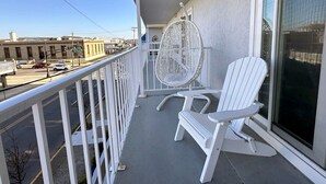 Un balcon avec deux fauteuils Adirondack blancs, un fauteuil en osier et une grande fenêtre.