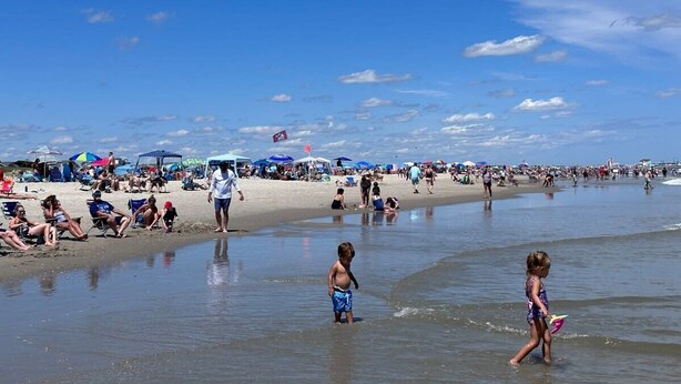 Une plage bondée, avec des gens, des parasols et des chaises de plage.