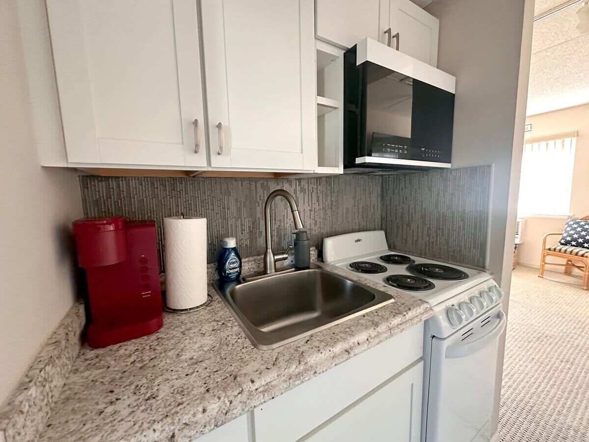 A compact kitchen with a stainless steel sink, a stove, and white cabinets.