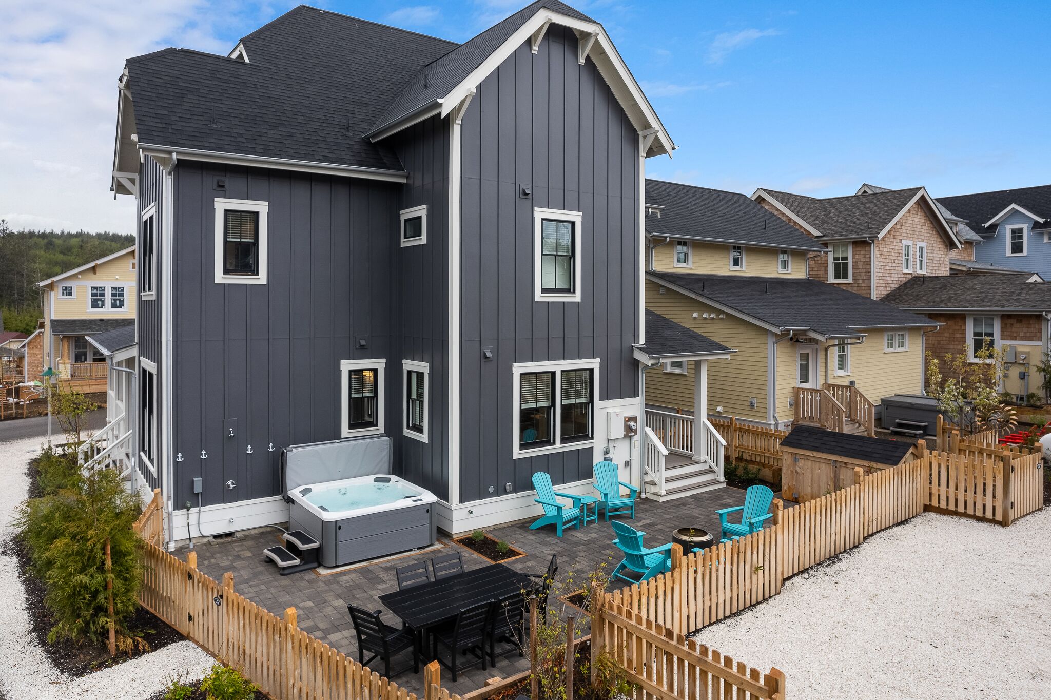 A two-story house with a patio area featuring a hot tub, outdoor seating, and a fenced garden.