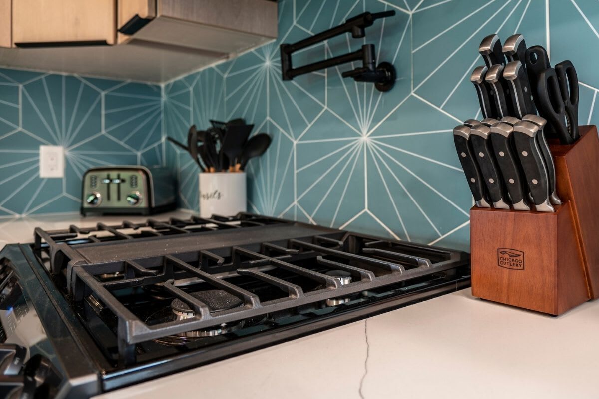 Una cocina con estufa a gas, bloque de cuchillos y soporte de pared para cuchillos.
