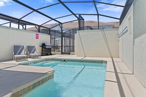 An indoor swimming pool with a glass enclosure, a barbecue area, and lounge chairs.
