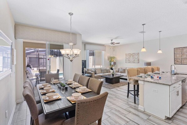 A spacious living area with a dining table set for six, a kitchen island, and a seating area with sofas.