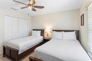 Et hotelværelse med to enkeltsenge, en ventilator i loftet, et natbord med lampe og et vindue med persienner.