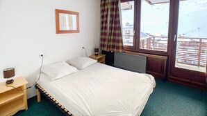 Una camera da letto con un letto, un comodino, una finestra con tende e vista sugli edifici.