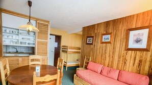 Una stanza compatta con un letto a castello in legno, un tavolo da pranzo con sedie, un angolo cottura e una zona salotto accogliente con un divano.