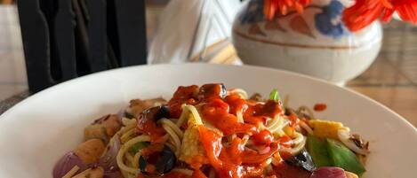 A plate of pasta with a tomato-based sauce, vegetables, and chicken, set on a table with a woven placemat.