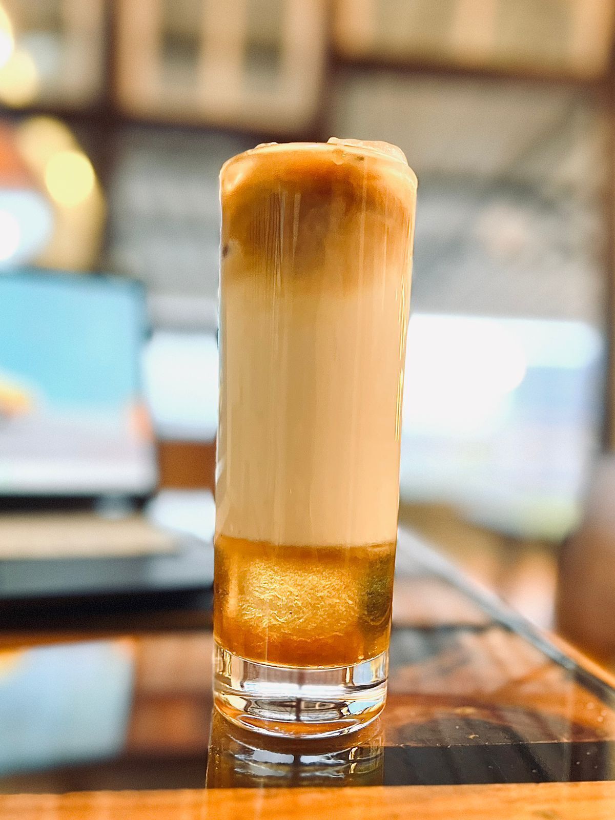 A tall glass of layered beverage on a reflective surface.