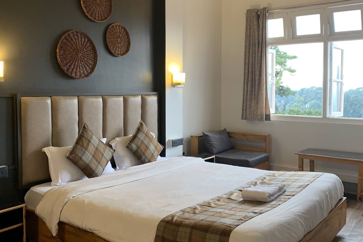 A bedroom with a large bed, a headboard with a padded design, wall-mounted decorative items, a bedside table, and a window with curtains.