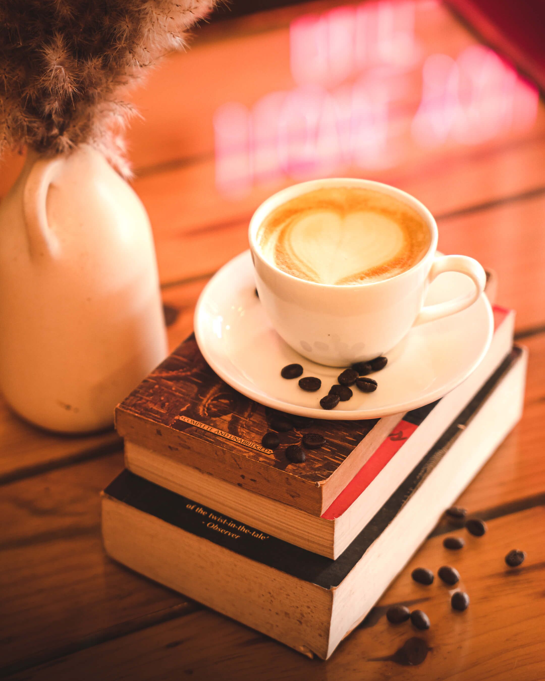 Una taza de café sobre un plato con un diseño de corazón, colocada encima de una pila de libros.