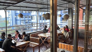 An indoor dining area with wooden tables and benches, large windows, and hanging light fixtures. - The Living Roof (Shillong)