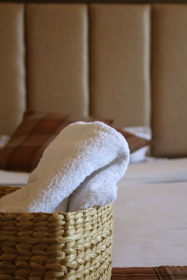 A wicker basket with a white towel on a bed with a headboard and a brown pillow.
