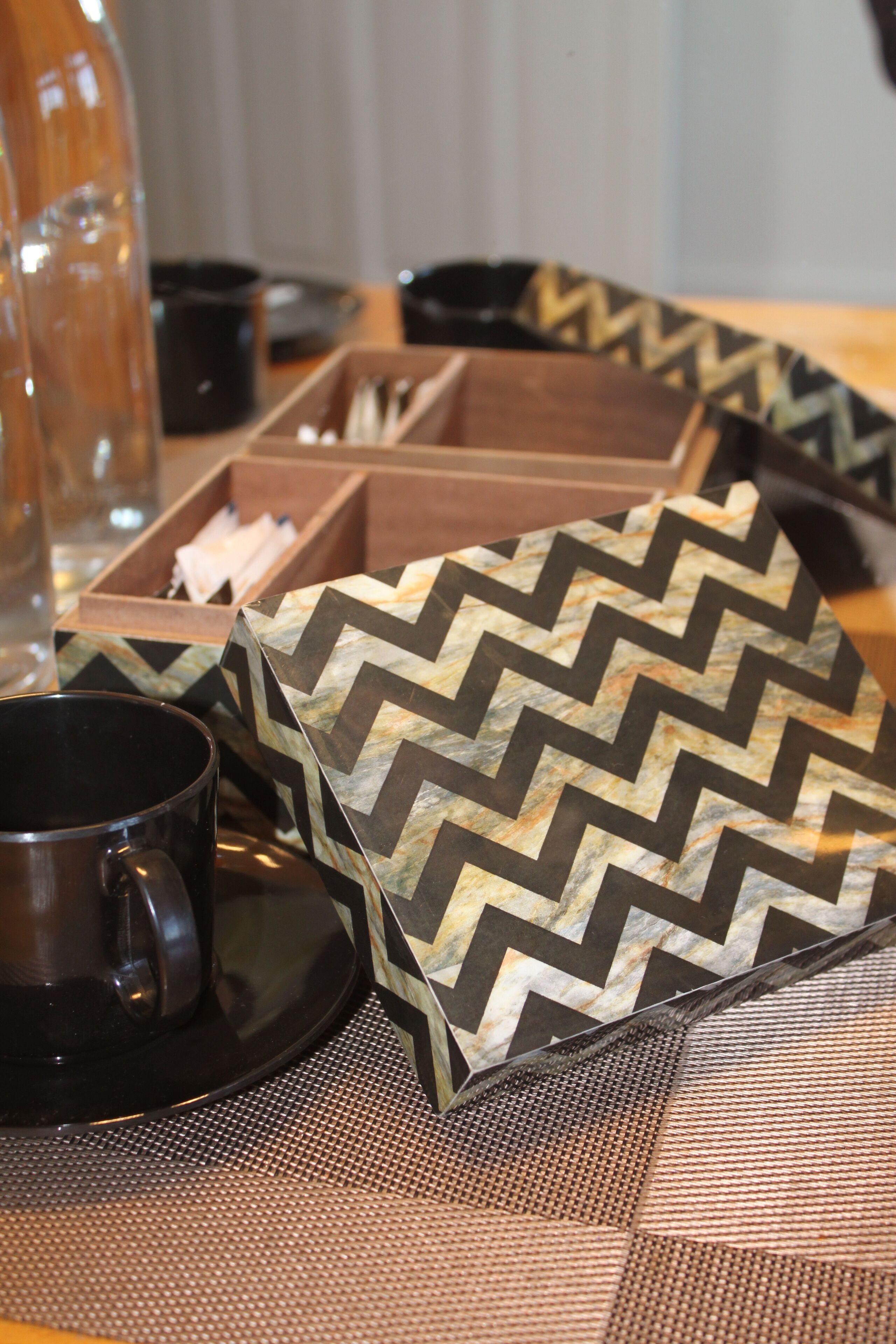 A table with a black mug, a patterned box, and a wooden tray.