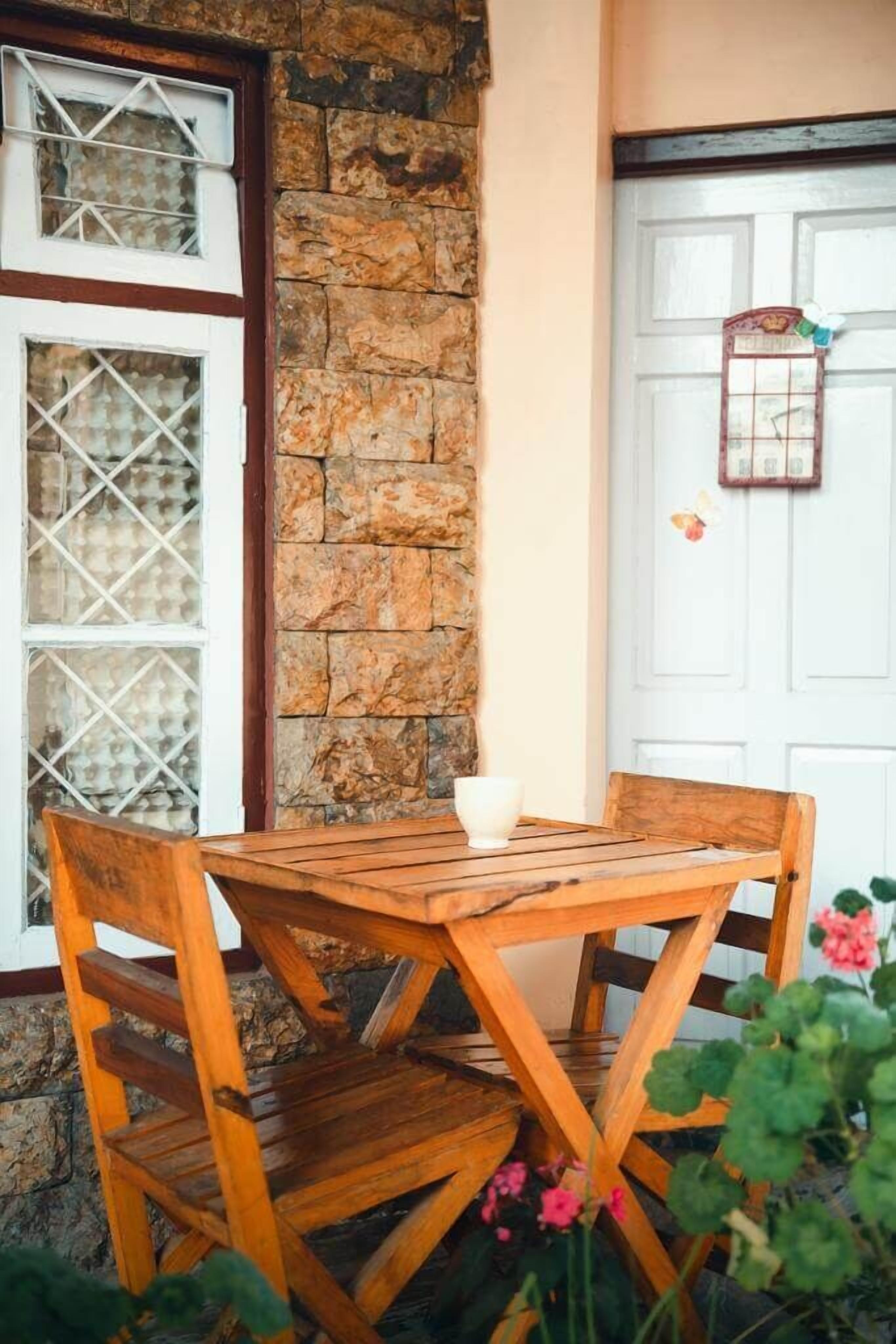 A wooden table and chairs set against a stone wall with a white door and window with decorative elements.