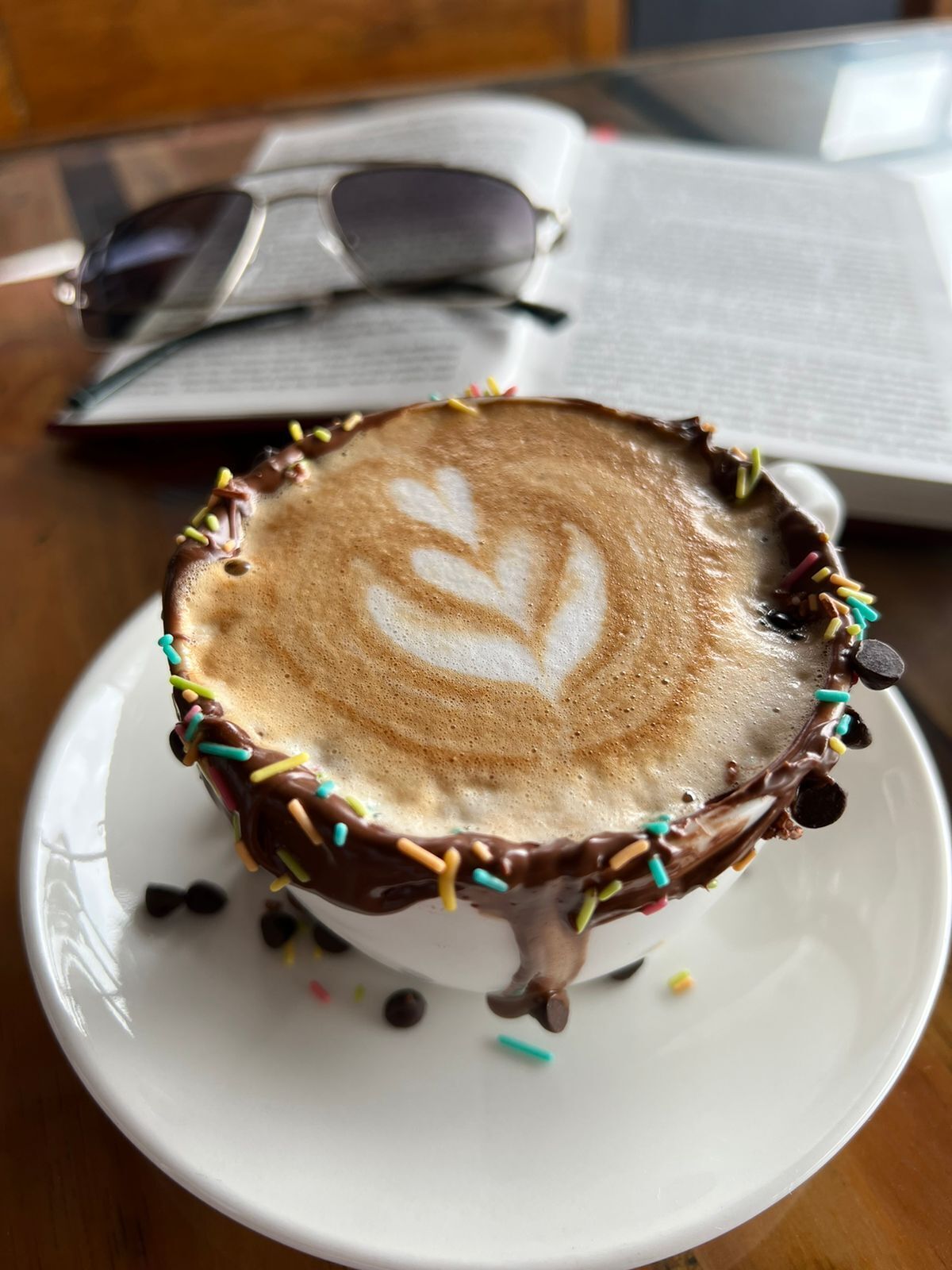 Een kop koffie met chocoladesaus en sprinkles op een wit bord.