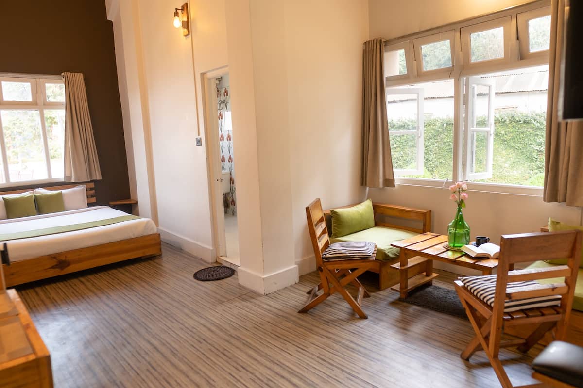A cozy room with a bed, a seating area with chairs and a table, and large windows with curtains.