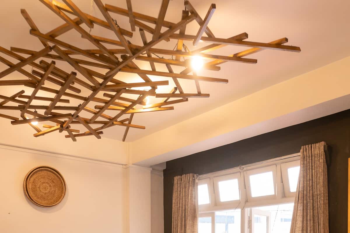 A single-bed room with a wooden floor, a wooden headboard, a bedside table, and a window with curtains.
