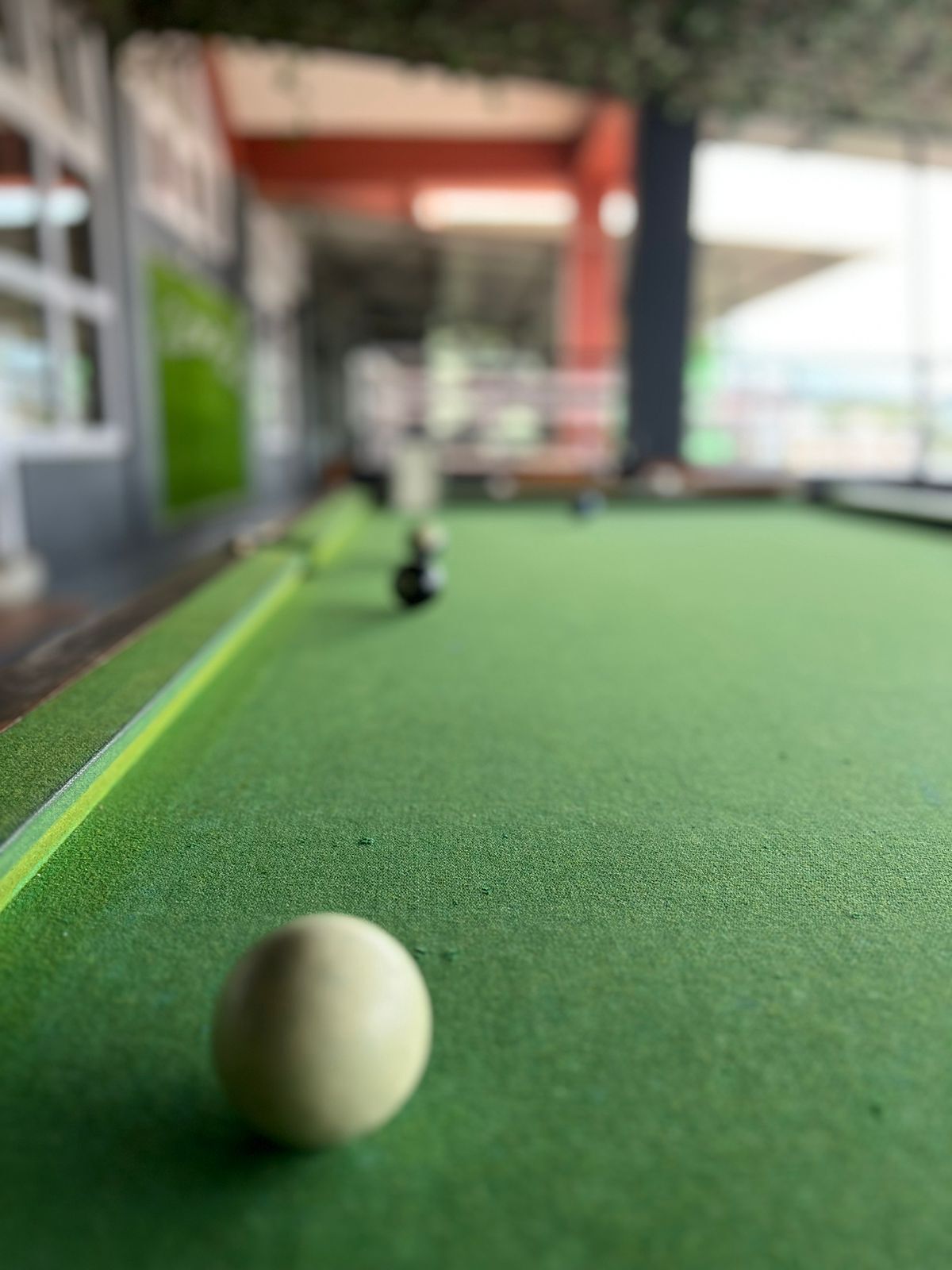 A close-up of a pool table with a single white cue ball in focus, and a blurred background suggesting an indoor setting with a green felt surface.