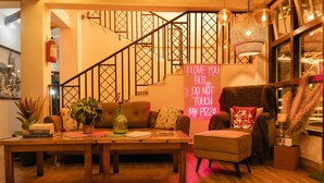 A cozy living room with a staircase, a wooden table with books and a plant, and a neon sign. - The Living Roof (Shillong)